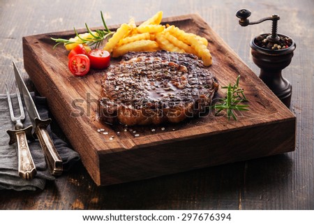 Medium rare grilled Steak Ribeye Black Angus with french fries on serving board block on wooden background