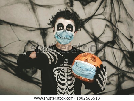 
Happy Halloween,kid wearing medical mask in a skeleton costume with halloween pumpkin over gray background

