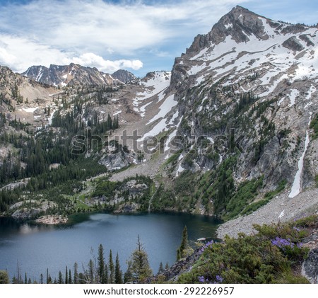 Alpine Lake in the Idaho Sawtooth Wilderness with snow covered mountain peaks surrounding blue water.