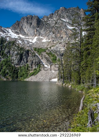 Alpine Lake in the Idaho Sawtooth Wilderness with snow covered mountain peaks surrounding clear water.