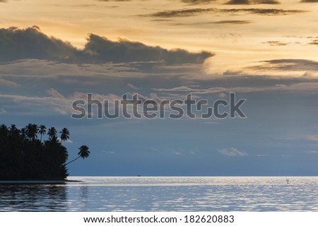 Tropical Island Sunset. An uninhabited island seen in the remote and exotic Maluku area of Indonesia with palm trees and white sandy beaches. Also known as the 