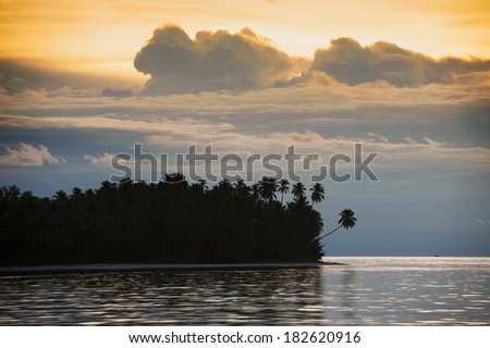 Tropical Island Sunset. An uninhabited island seen in the remote and exotic Maluku area of Indonesia with palm trees and white sandy beaches. Also known as the \