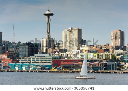 Seattle Waterfront. A sailboat on Elliott Bay passes in front of the waterfront and the Space Needle in the background.