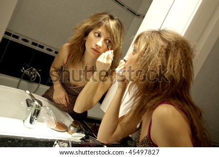 Beautiful Young Woman Making Up wiyh Concealer in front of the Dresser