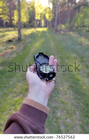A man holding the compass in his hand and aiming the direction in the forest.