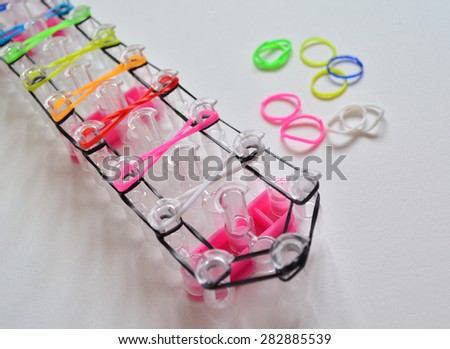 Colorful nails making a rubber loom bracelet with a hook . Hands close up. Young fashion concept.