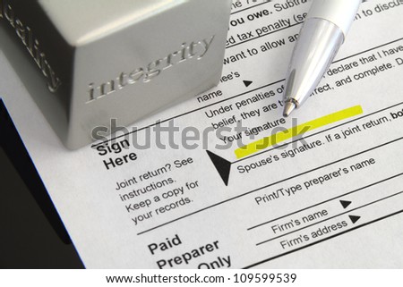 Tax form with signature field highlighted, ink pen, and an integrity paper weight.