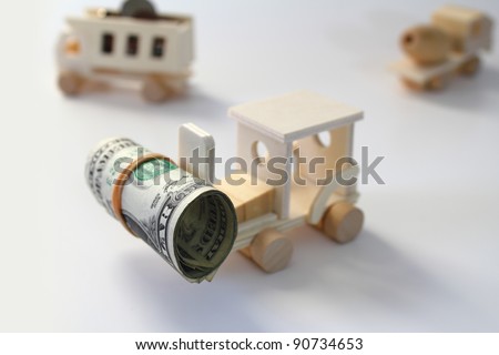 Toy, wooden forklift lifting a roll of money with dump truck and cement truck in the background.