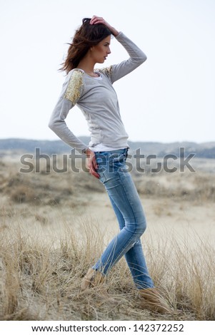 Beautiful young woman wearing a grey shirt and jeans posing in the dunes