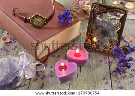 Still life with lilac candles and clock on old book