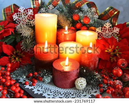 Festive burning candles with traditional Christmas decorations, conifer branches, berries and baubles on plate with white napkin. Christmas and New Year celebratory still life.