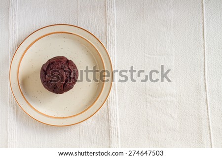 Chocolate muffin on beige plate over light fabric table cloth background with text space on right side.