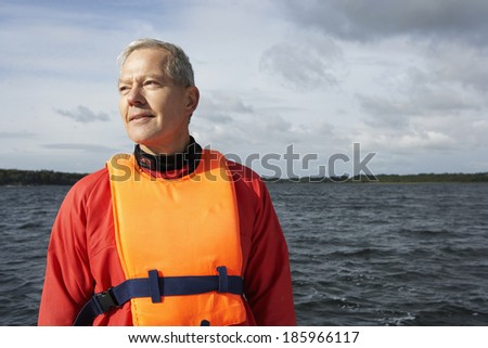 Senior man wearing life jacket by lake