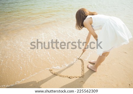 Woman drawing a heart in the sand in shallow water
