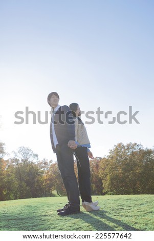 Couple standing back to back on the grass