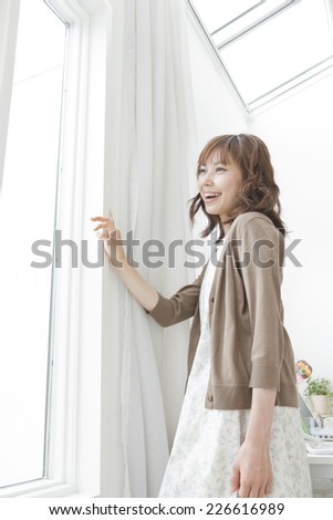 Young woman looking outside through an open curtain