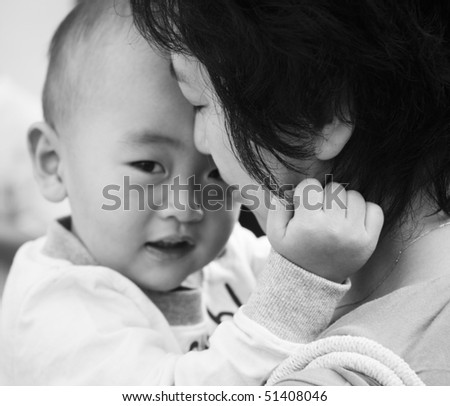 young asian mother holding her 2-year old son with eyes closed; black and white.