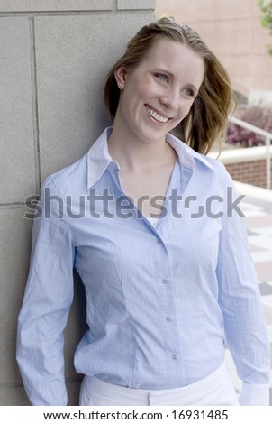 Adult female in blue collared shirt smiling while standing against a concrete wall