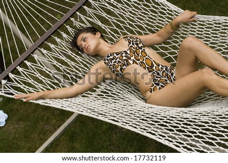 Photo of an adult female\'s clothed body laying on a white hammock on a sunny day