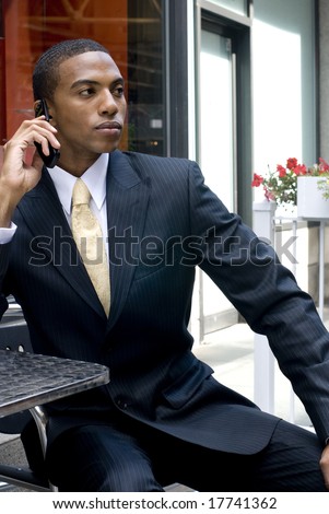Good looking black man with yellow tie and dark suit on cell phone on sunny day