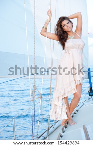 A flawless woman wearing a white, draped, high-low dress on a boat.