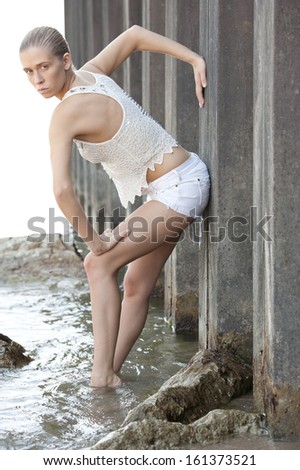Attractive model wearing all white posing near a steel beam at the beach.