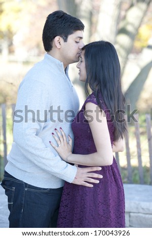A young and happy Indian man kissing his fiance on the forehead on a sunny day in the Fall.