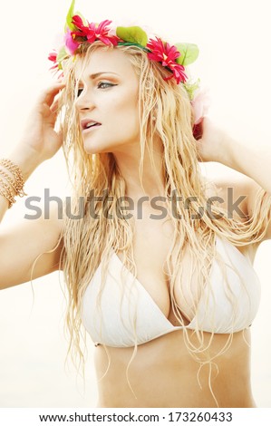 An attractive young female model wearing a flower crown and a white bathing suit at the beach.