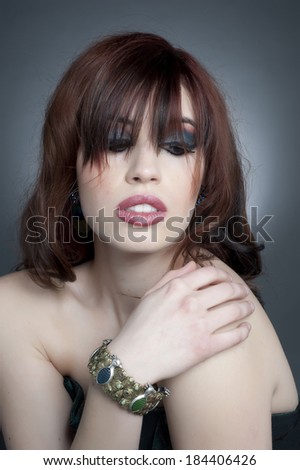 A young female model posing with her hand on her shoulder in a studio.