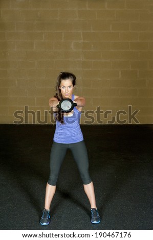 A young and athletic trainer posing with a kettlebell in a gym.