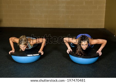 Two athletic trainers doing a push up on a bosu ball in a gym.