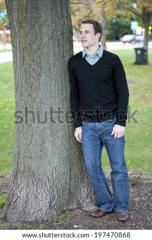 An attractive, fashionable and young male model posing outdoors on a sunny day looking left.
