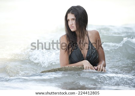 A young brunette female model posing in a wet dress at the beach on a sunny day.