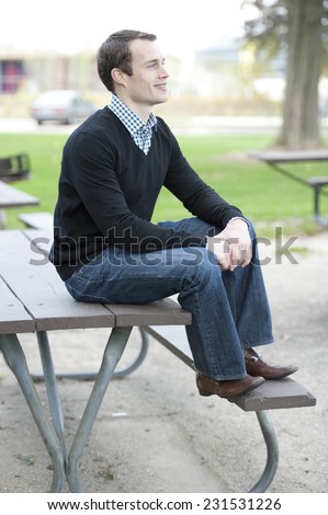 Young white male sitting on an outdoor table in the park on a sunny day.