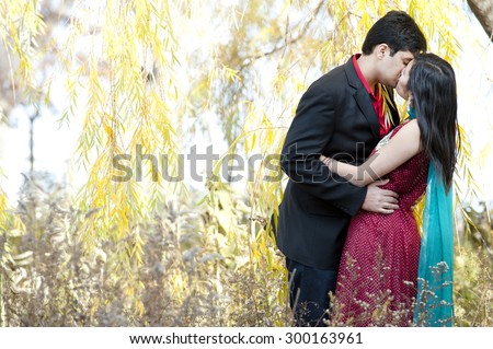 A young and happy Indian couple kissing under a willow tree in the Fall on a sunny day.