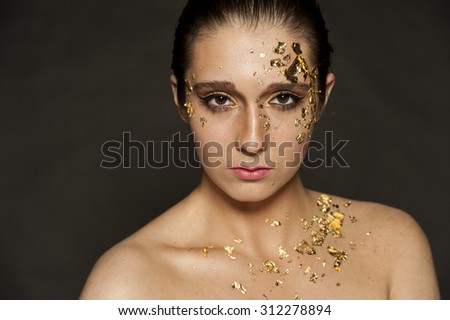 Gorgeous brunette female portrait with gold flakes on her face and hair in a bun on a black background.