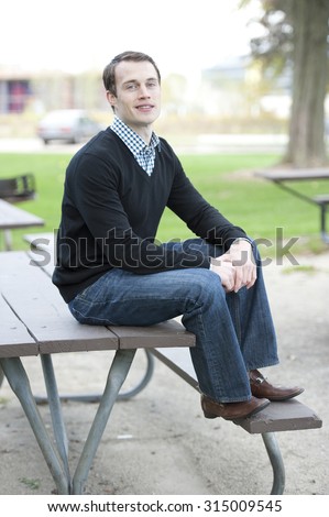Happy young white male model posing outdoors while sitting on a table.