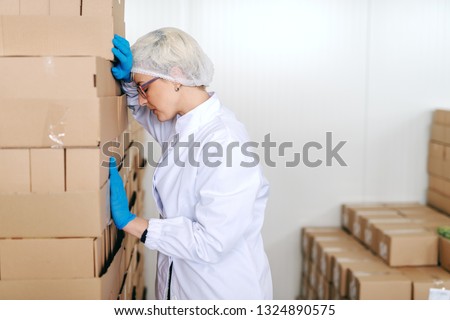 Desperate blonde female employee in sterile uniform leaning on boxes. Food factory interior. Stock photo © 