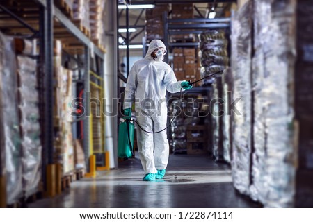 Man in protective suit and mask disinfecting warehouse full of food products from corona virus / covid-19.