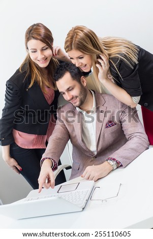 Business, technology, teamwork and people concept - smiling business team with laptop computers having discussion over office background.