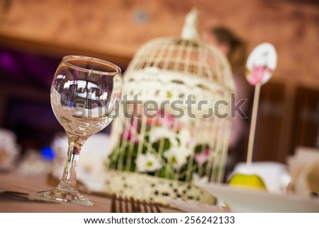 Wedding table decoration at restaurant. Shallow depth of field. Glass of wine with cage bird out of focus at background.