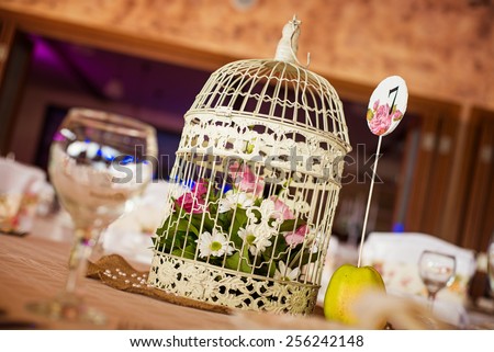 Wedding table decoration at restaurant. Shallow depth of field. Cage bird with flowers inside.