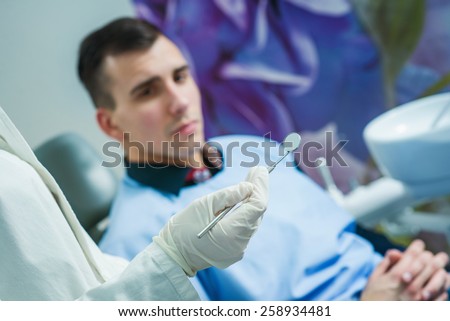 Close up of dentist tool, frightened patient in the background. Dentist office.