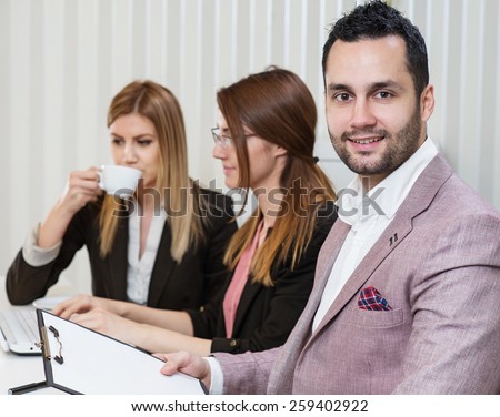 Portrait of businessman at busy office, two beautiful business woman in background.