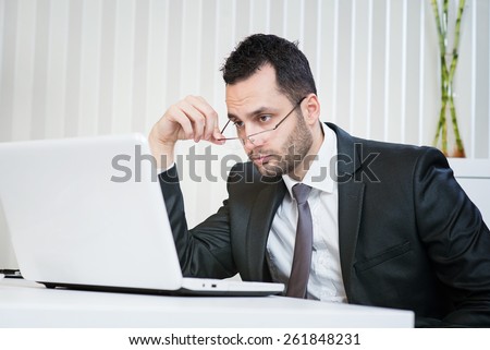 Confused businessman looking at laptop at office. Resolving some problem.
