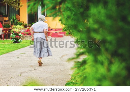 Old grandmother walking with crutch on she\'s back. Retirement.
