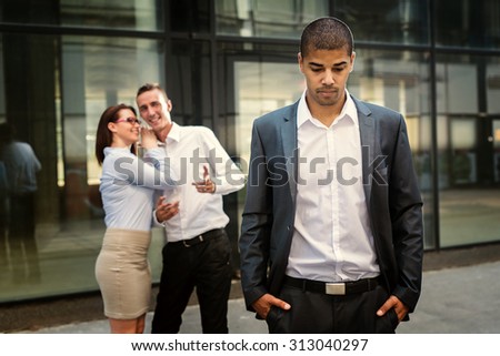 Gossip colleagues in front of their office, handsome businessman portrait and gossip out of focus in background.