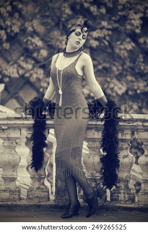Black-and-white retro style depiction of a woman in typical style of the 1920s or 1930s. She\'s fashionably adorned in black lace, pearls, evening gloves and a pearl-accented wrap-around headpiece.
