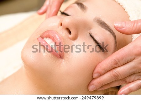 Close-up of young relaxing beautiful woman having facial massage with massage oil