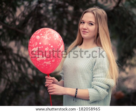Open portrait of the young woman the beautiful woman in cold weather in park. The sensual blonde poses and is cheerful with a red balloon.